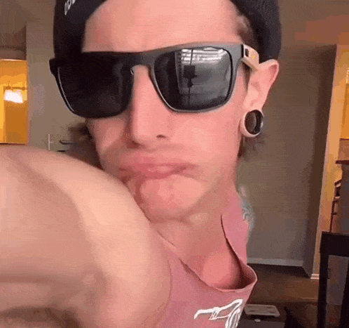 a young man wearing sunglasses and a hat is making a face .