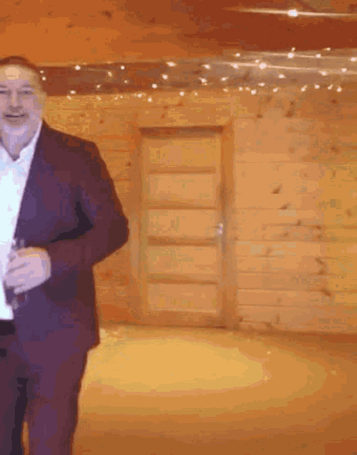 a man in a suit is holding a glass in front of a wooden wall