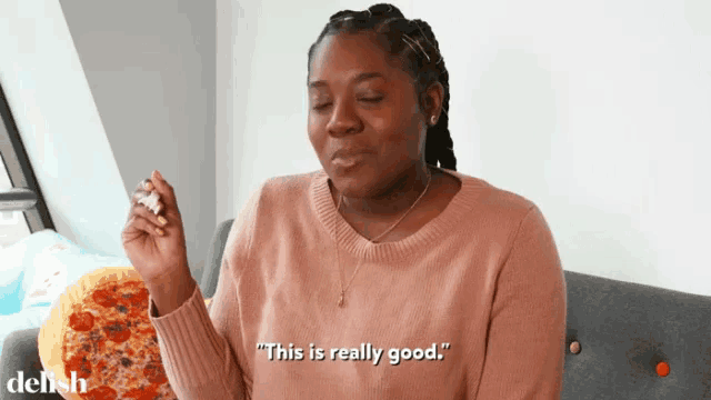a woman in a pink sweater is sitting on a couch and says " this is really good "