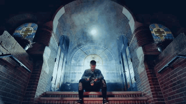 a man sits on a set of stairs with a stained glass window behind him