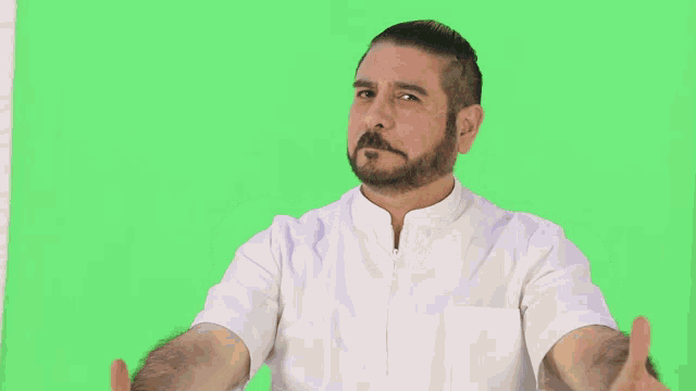 a man with a beard is wearing a white shirt with his arms outstretched in front of a green screen .