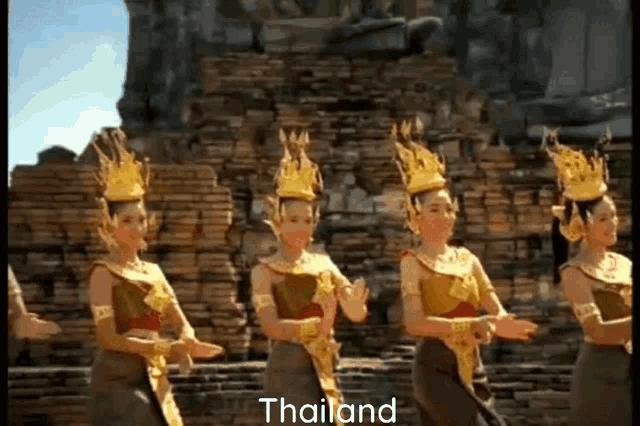 a group of women are dancing in front of a brick wall and the word thailand is on the bottom right