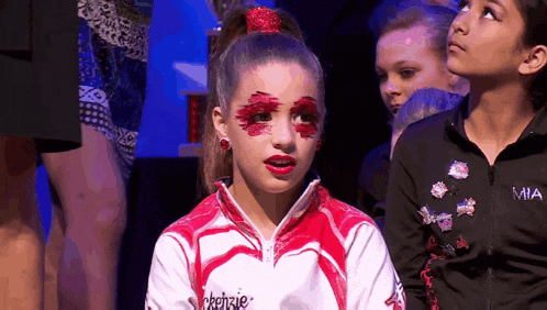 a girl with red paint on her face is wearing a jacket with the word mia on it