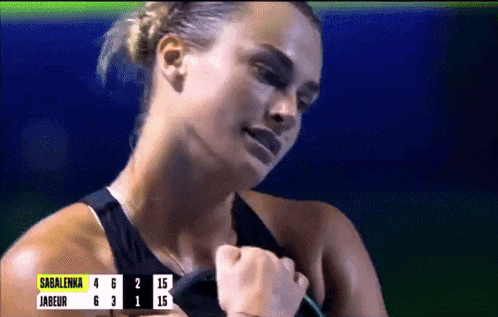 a woman in a black tank top holds her fist in front of a scoreboard that says sagalenka