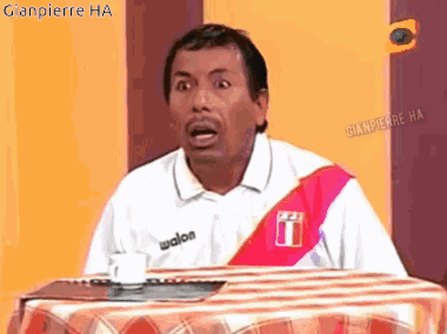 a man wearing a walon shirt sits at a table with a cup of coffee