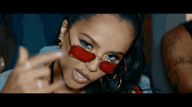 a woman wearing red sunglasses and hoop earrings giving the middle finger