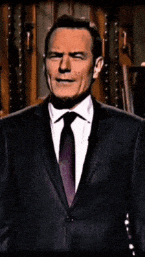 a man in a suit and tie stands in front of a wooden wall