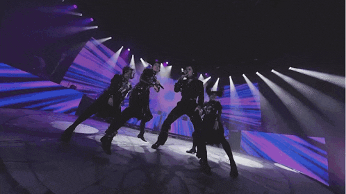 a group of people dancing on a stage with purple lights