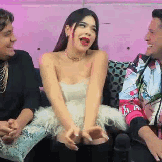 a woman in a white dress is sitting on a couch with two men and laughing .