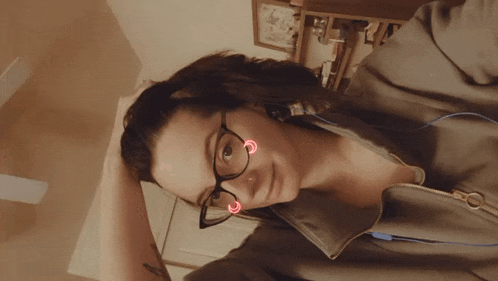a woman wearing glasses has a tattoo on her arm and is smiling
