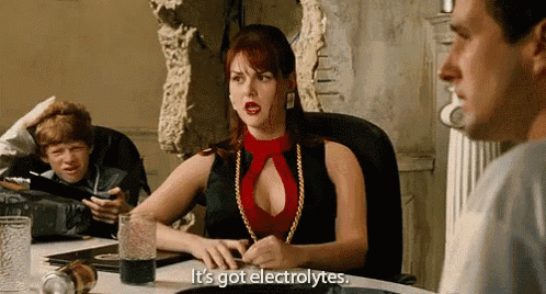 a woman in a red top is sitting at a table with a glass of water and says it 's got electrolytes .