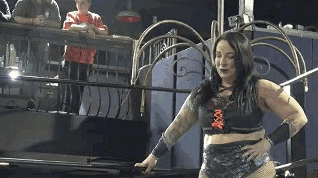 a woman is standing in a wrestling ring with her hands on her hips and a crowd watching .