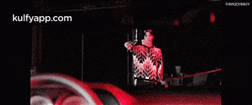 a man is singing into a microphone in a dark room with the website kulfyapp.com at the bottom