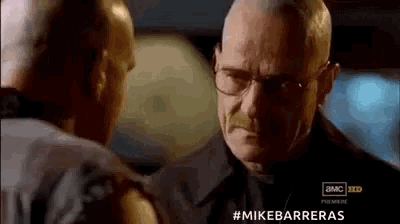 two men are standing next to each other and looking at each other . one of the men is wearing glasses .