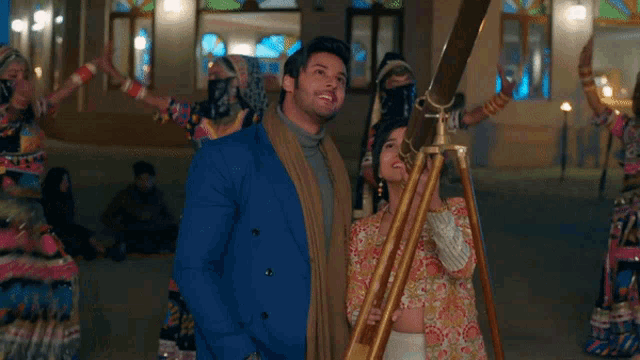 a man in a blue suit stands next to a woman looking through a telescope ..