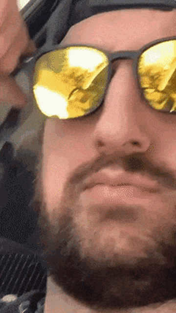 a man with a beard wearing sunglasses and a hat looks at the camera