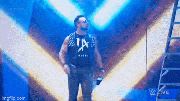 a man in a la shirt is standing on a stage holding a microphone and a bottle of beer .