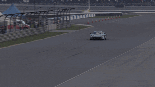 a race car is driving down a track with a few people watching