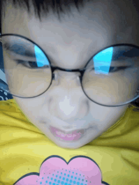 a young boy wearing glasses and a yellow shirt with a pink heart on it