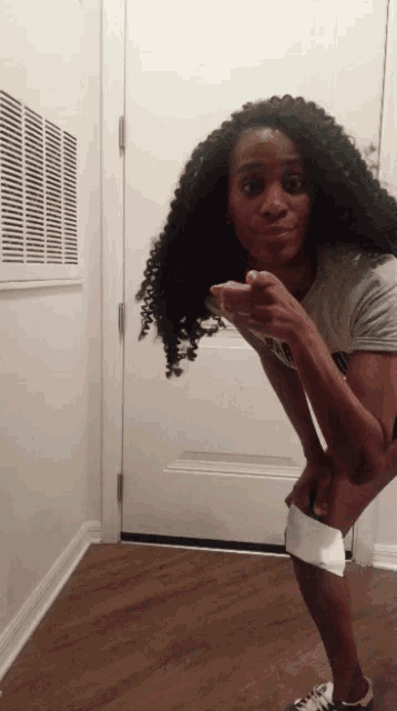 a woman with curly hair is standing in front of a white door and pointing at the camera