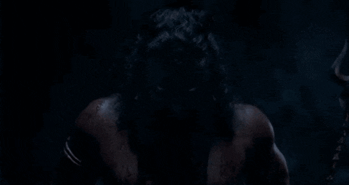 a man with a beard and long hair is standing in the dark with blood on his face .