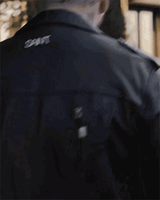 a man with a beard is wearing a black leather jacket and standing in front of a window .