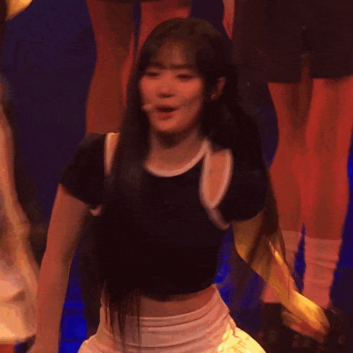 a girl in a black crop top and white skirt is dancing on stage