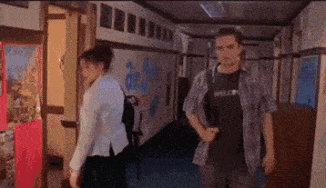a man and a woman are walking down a school hallway .