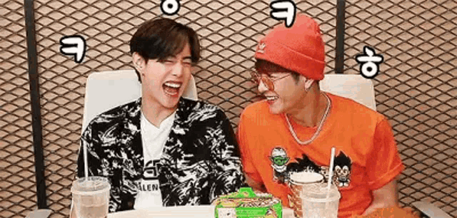 two young men are sitting at a table laughing .