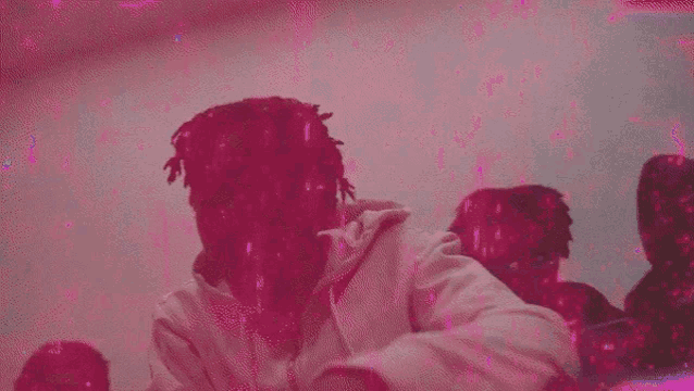 a man with dreadlocks is sitting in front of a crowd of people in a pink room .