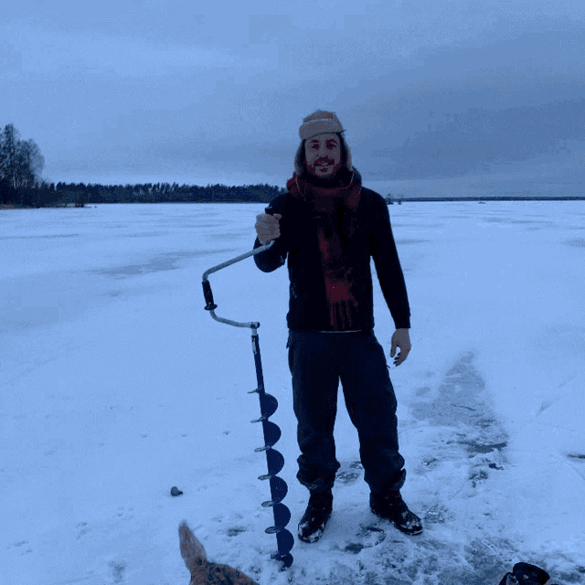 a man is standing in the snow holding a fishing drill