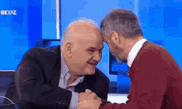 two men are sitting at a table with their hands on each other 's faces .