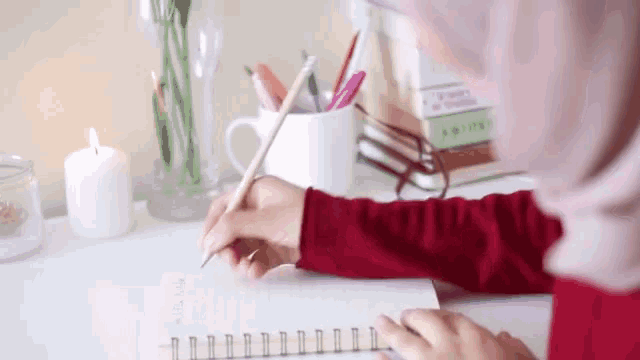 a woman in a red hijab is writing in a notebook