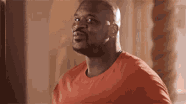 a bald man in an orange shirt is looking up at something .