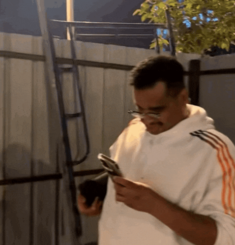 a man wearing glasses and a white adidas sweatshirt looks at his phone