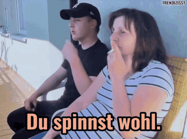a man and a woman are sitting on a bench and the woman is smoking a cigarette and says du spinnst wohl