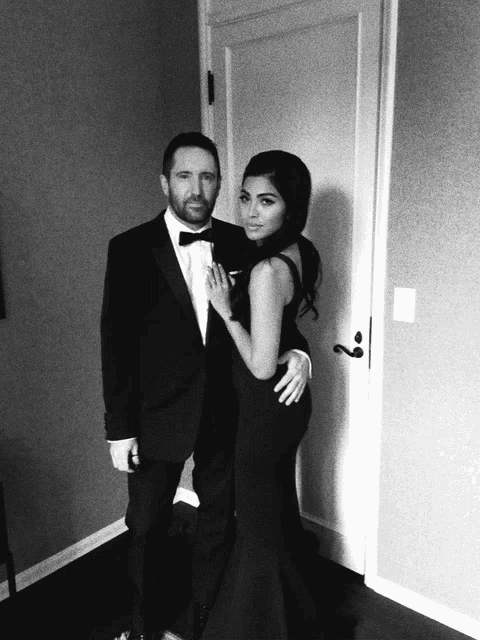 a man in a tuxedo and a woman in a black dress pose for a photo