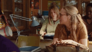 a woman is sitting at a desk in a classroom with a lamp .