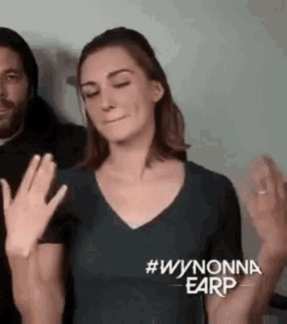 a woman in a black shirt is making a funny face while a man looks on .