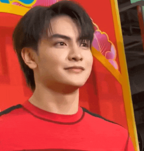 a young man wearing a red shirt is standing in front of a red wall