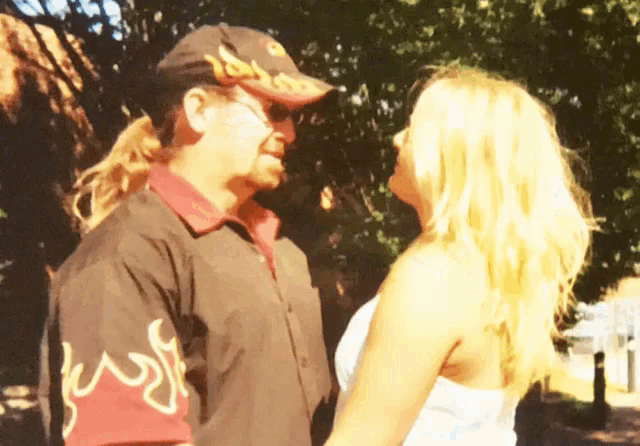 a man in a brown shirt with flames on the sleeves kisses a blonde woman