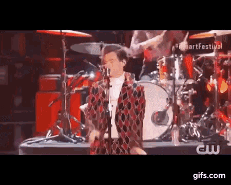 a man is singing into a microphone on a stage with a drum set .