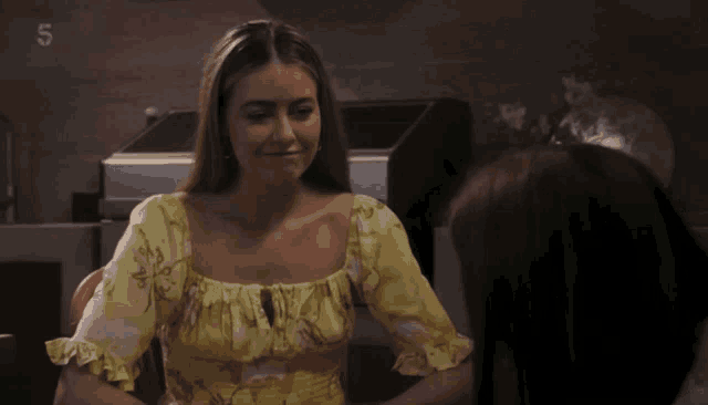 a woman in a yellow floral top talks to another woman with the number 5 on the bottom