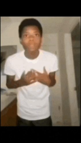 a young man in a white shirt is standing in a room with his hands folded in front of his chest .