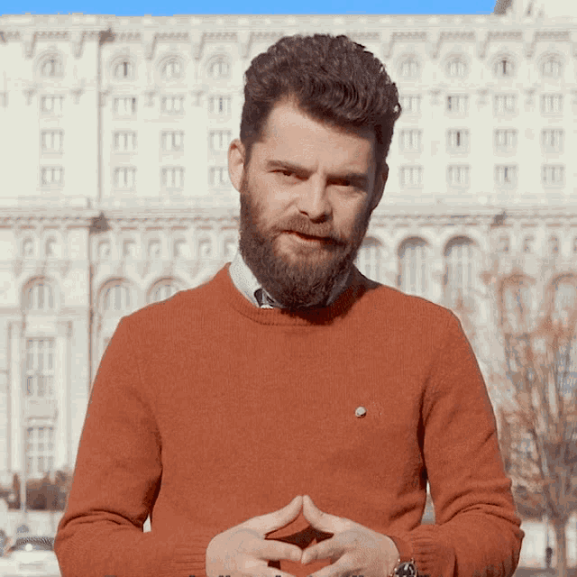 a man with a beard wearing an orange sweater and a watch