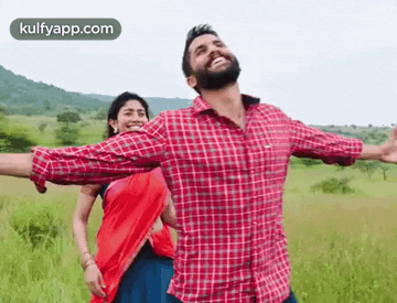a man in a plaid shirt is standing next to a woman in a red sari in a field .