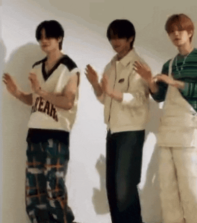three young men are standing next to each other and clapping their hands in front of a white wall .