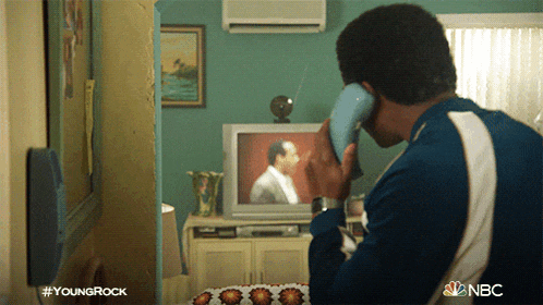 a man is talking on a phone in front of a television with a nbc logo on the bottom