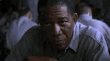 a man is sitting at a table in a prison cell eating a piece of food .
