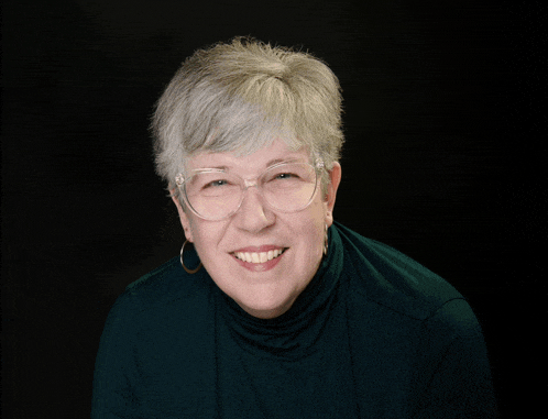 a woman wearing glasses and a green turtleneck smiles